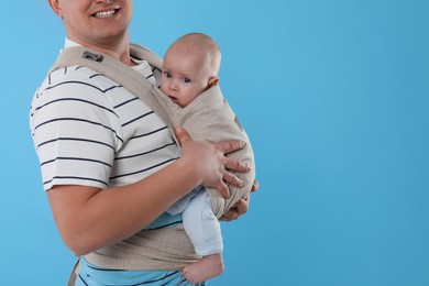 Photo of Father holding his child in sling (baby carrier) on light blue background, closeup. Space for text
