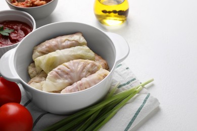 Photo of Ceramic pot with uncooked stuffed cabbage rolls and ingredients on white table, closeup. Space for text