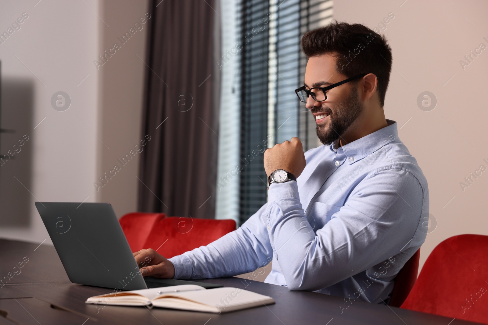 Photo of Happy young man working on laptop at table in office