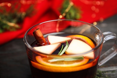 Photo of Tasty mulled wine with spices in glass cup on wooden table, closeup