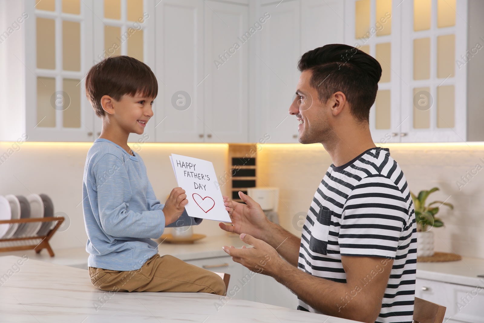 Photo of Little boy greeting his dad with Father's Day in kitchen