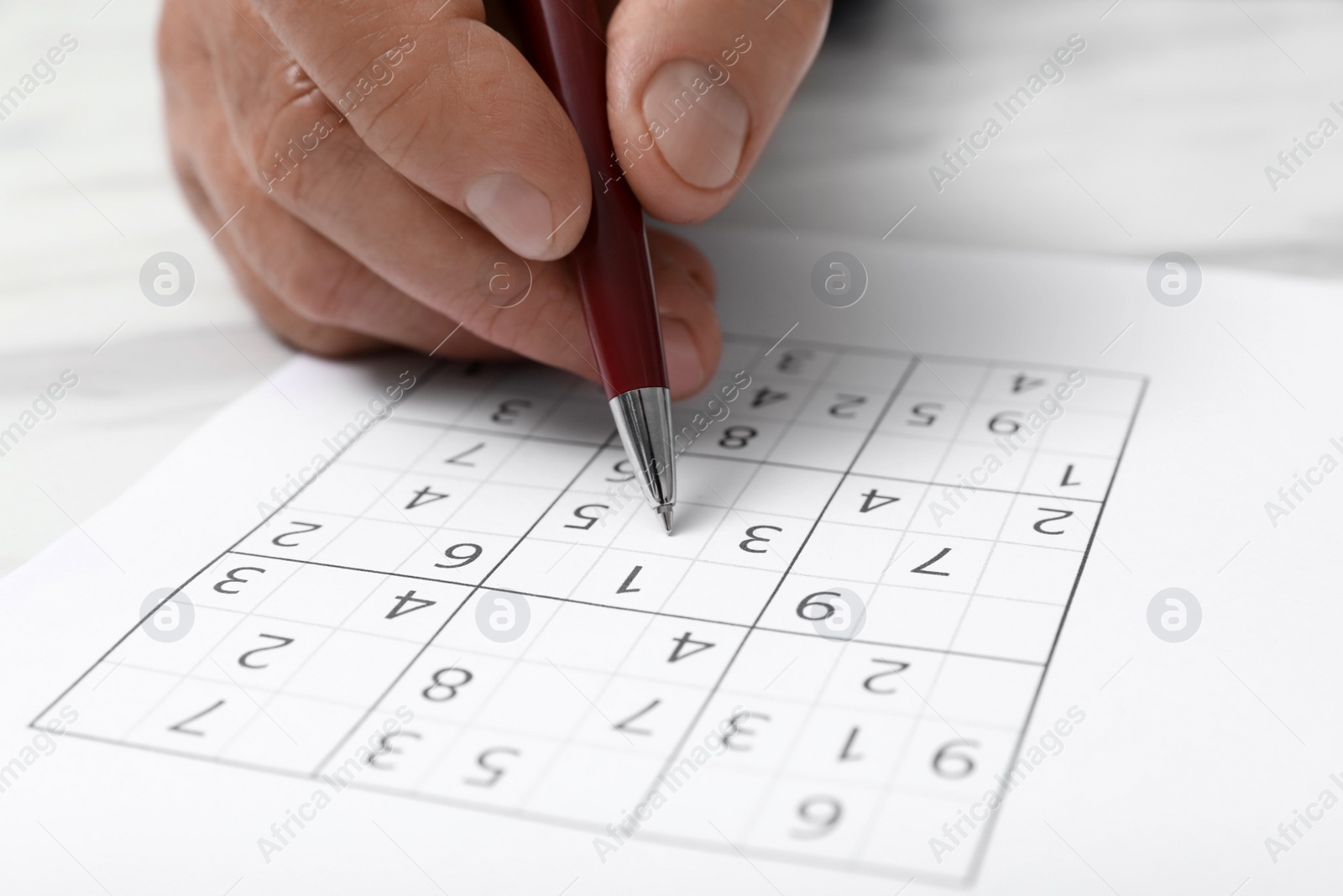 Photo of Senior man solving sudoku puzzle at white table, closeup