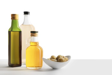 Bottles of different cooking oils and olives on white background, space for text