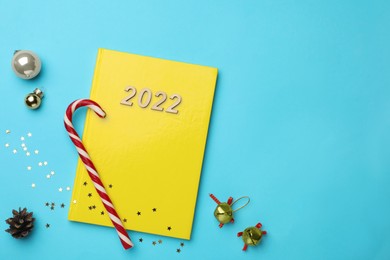 Photo of Yellow planner and Christmas decor on light blue background, flat lay. Space for text. Planning for 2022 New Year
