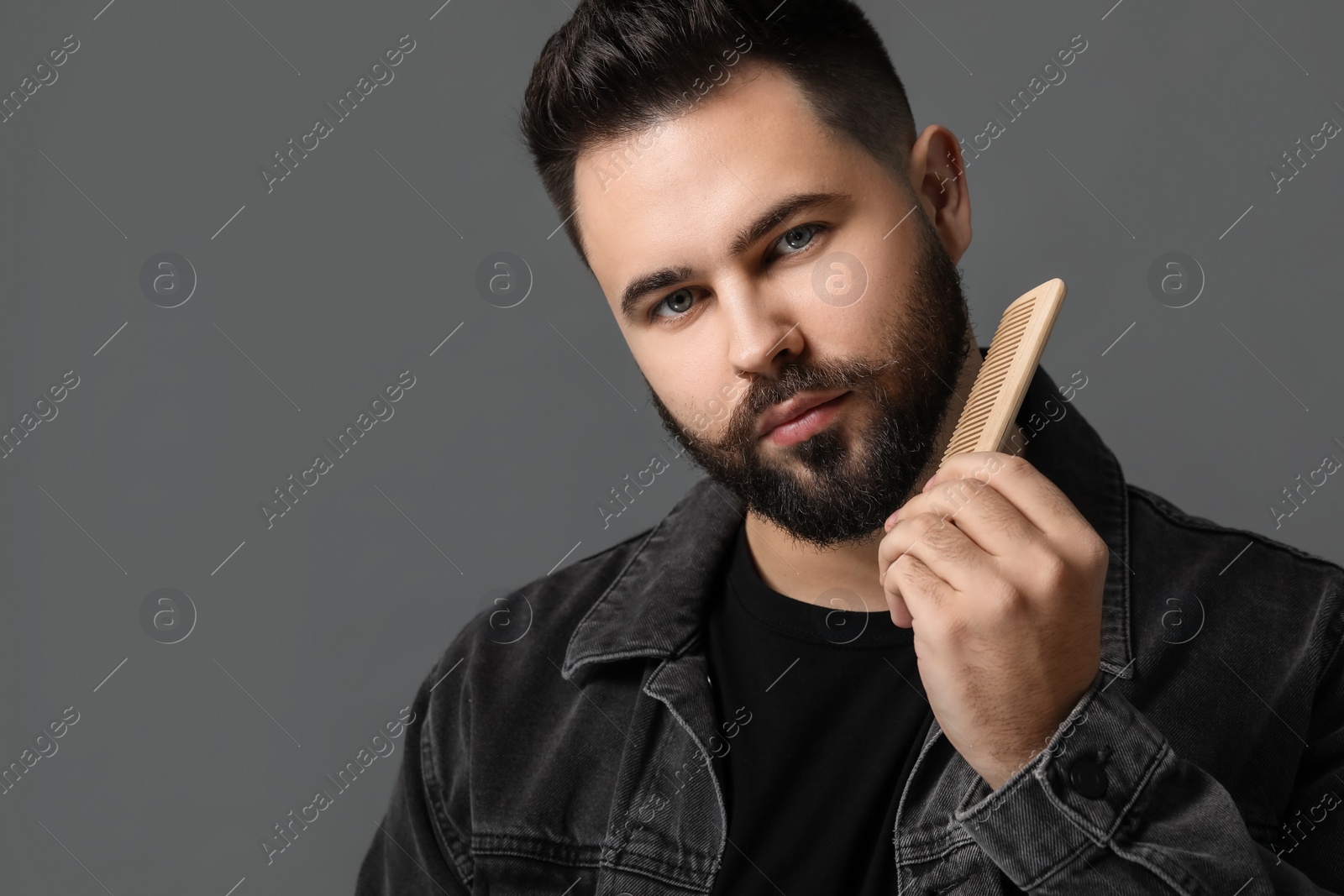 Photo of Handsome young man combing beard on grey background. Space for text