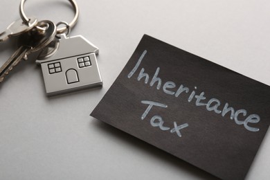 Photo of Card with phrase Inheritance Tax and keys with house shaped key chain on grey background, closeup