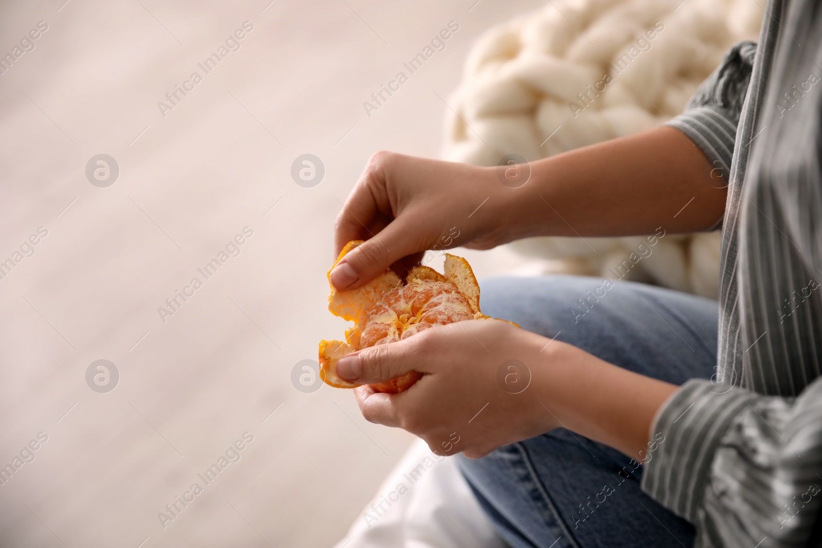 Photo of Woman peeling fresh tangerine on blurred background, closeup