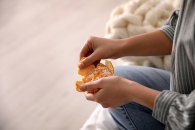 Woman peeling fresh tangerine on blurred background, closeup