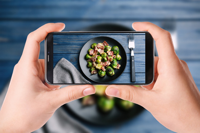 Image of Blogger taking picture of delicious Brussels sprouts with bacon at table, closeup. Food photography