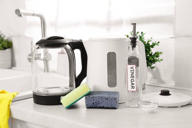 Photo of Cleaning electric kettle. Bottle of vinegar, sponges and baking soda on countertop in kitchen