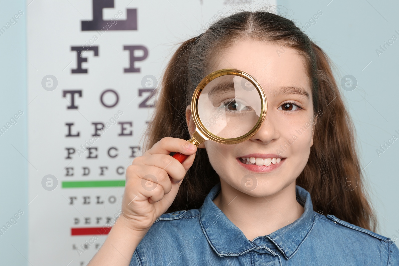 Photo of Cute little girl with magnifier in ophthalmologist office