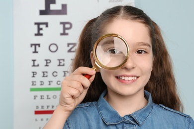 Photo of Cute little girl with magnifier in ophthalmologist office