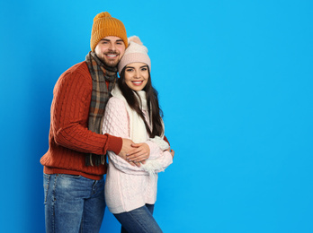 Happy young couple in warm clothes on blue background, space for text. Winter vacation