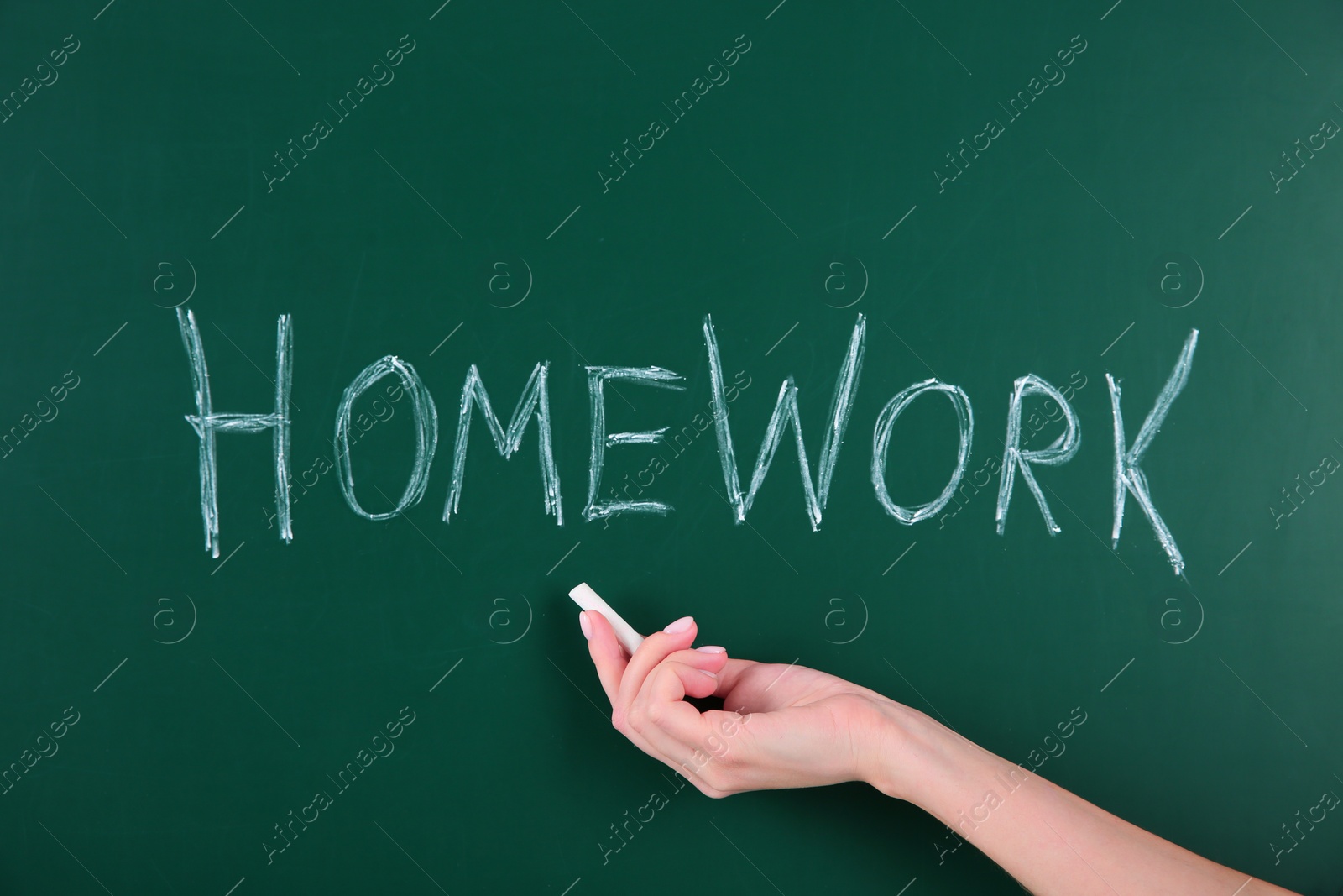 Photo of Woman writing word HOMEWORK on chalkboard, closeup