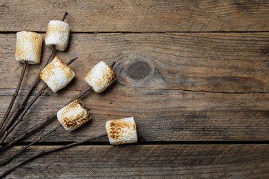 Photo of Twigs with roasted marshmallows on wooden table, flat lay. Space for text