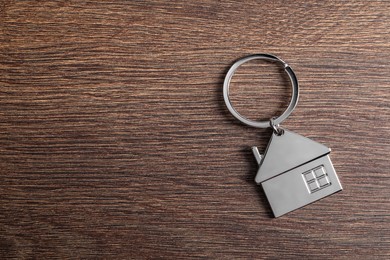 Photo of Metal keychain in shape of house on wooden table, top view. Space for text