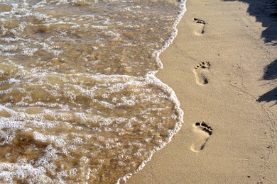 Photo of Sandy beach with footprints near sea on sunny day