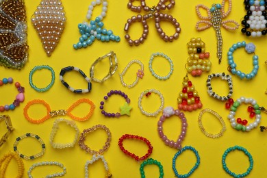 Photo of Beautiful handmade beaded jewelry and crafts on yellow background, flat lay