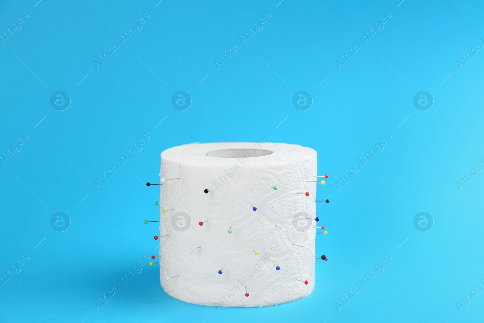 Photo of Roll of toilet paper with straight pins on light blue background. Hemorrhoid problems