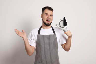 Photo of Excited confectioner in apron holding professional tools on light grey background