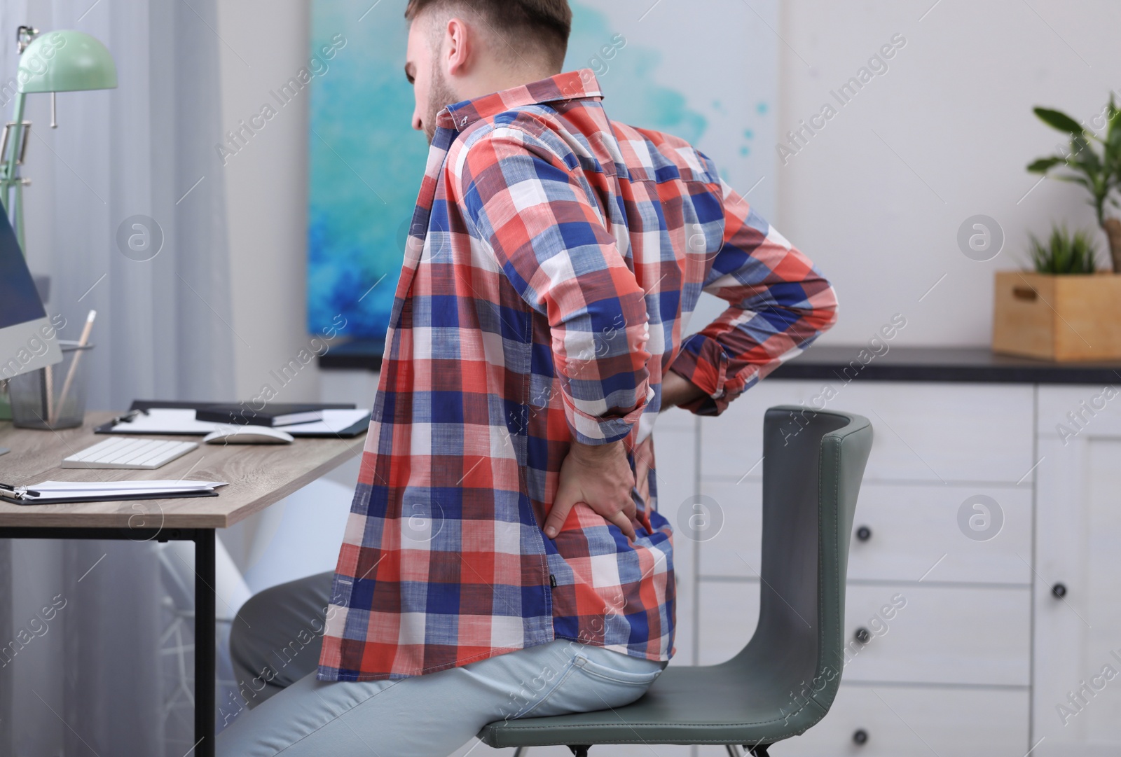 Photo of Young man suffering from back pain in office