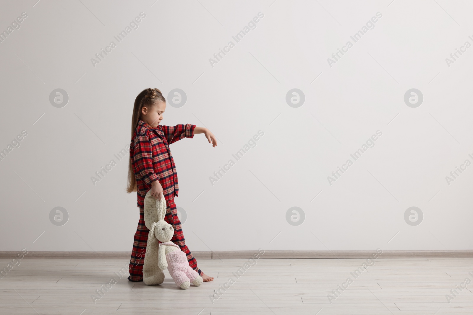 Photo of Girl in pajamas with toy bunny sleepwalking indoors, space for text