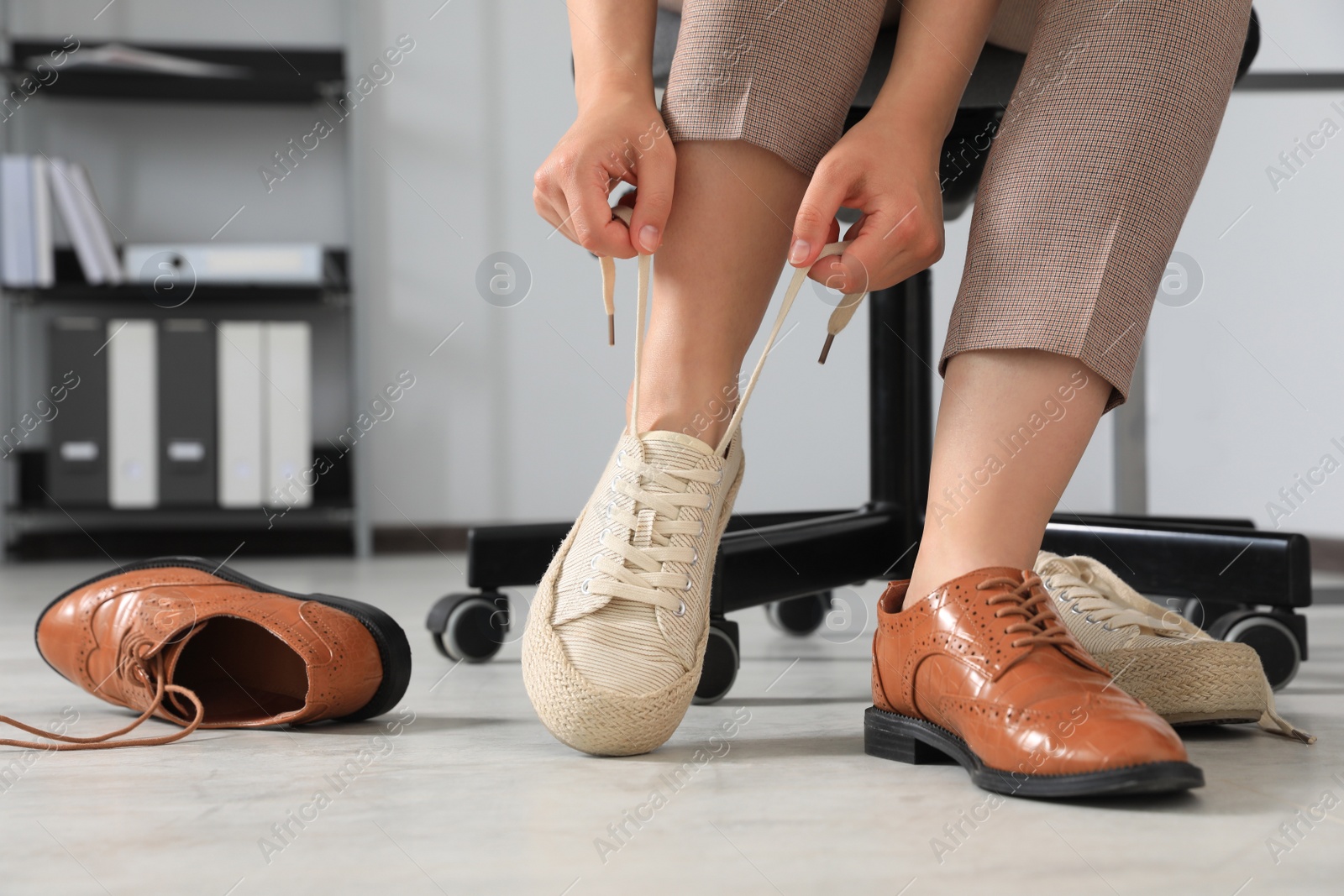 Photo of Woman taking off uncomfortable shoes and putting on sneakers in office, closeup