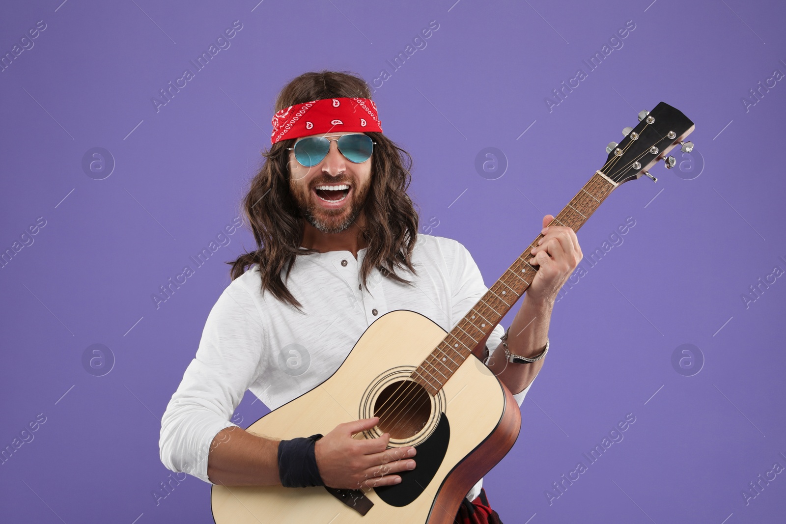 Photo of Stylish hippie man in sunglasses playing guitar on violet background