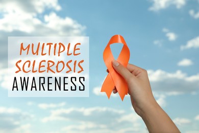 Image of Multiple Sclerosis Awareness Day. Woman holding orange ribbon against blue sky, closeup 