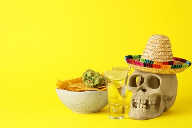 Photo of Mexican sombrero hat, human scull, tequila, nachos chips and guacamole in bowl on yellow background, space for text