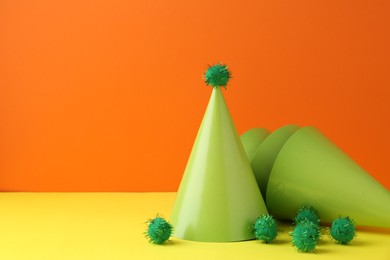 Party hats on yellow table against orange background, space for text