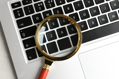 Photo of Magnifying glass and modern laptop on table, top view. Search concept
