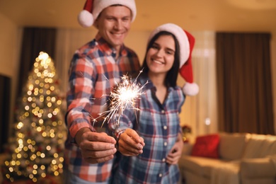 Couple holding sparkles in room decorated for Christmas, focus on fireworks
