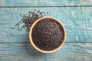 Bowl with uncooked black rice on blue wooden background, top view