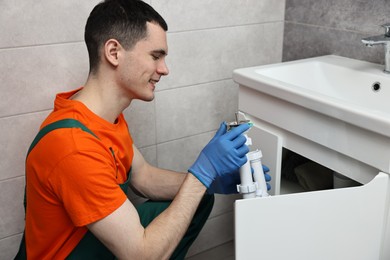 Photo of Smiling plumber wearing protective gloves repairing sink in bathroom