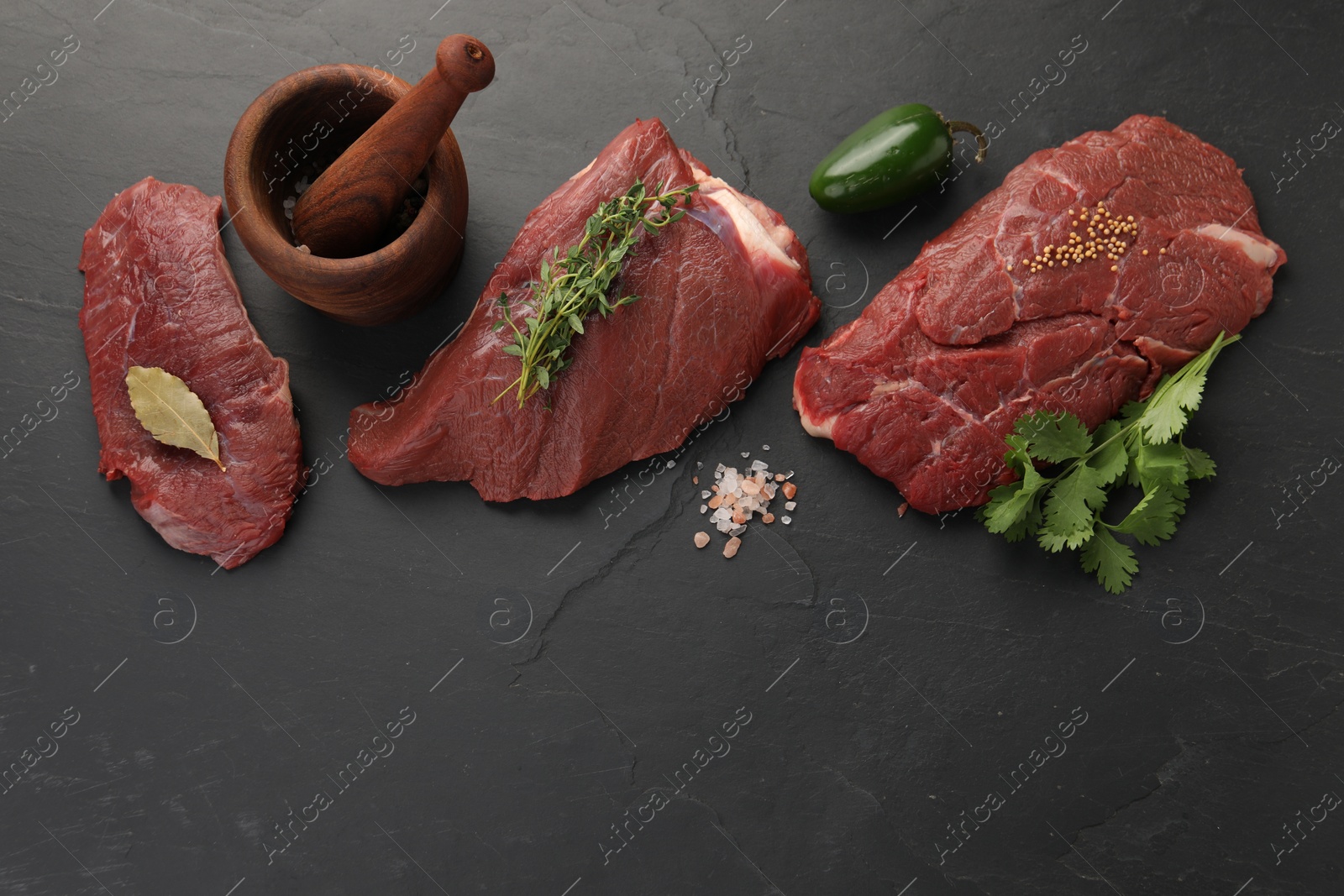 Photo of Pieces of raw beef meat, mortar with pestle and spices on black table, flat lay. Space for text