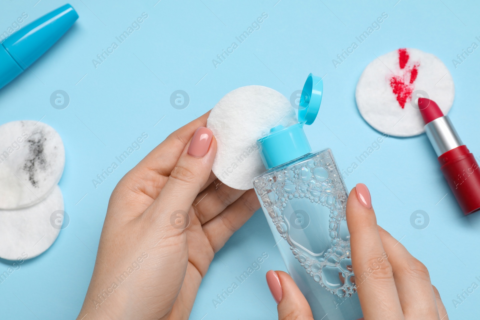 Photo of Woman using makeup remover, closeup. Cotton pads, lipstick and mascara on light blue background, top view