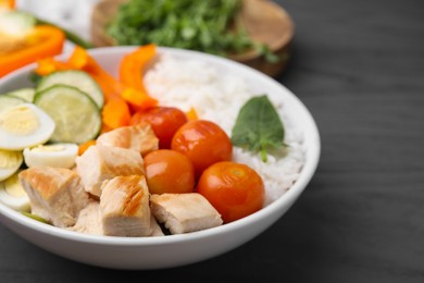 Delicious poke bowl with meat, rice, eggs and vegetables on black wooden table, closeup