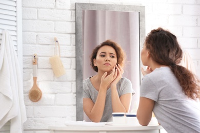 Photo of Beautiful young woman with acne problem looking in mirror at home
