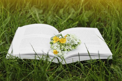 Photo of Open book with flowers on green grass outdoors