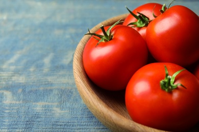 Photo of Ripe tomatoes in bowl on blue wooden table, closeup. Space for text