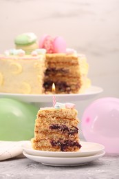 Piece of delicious cake with burning candle on light grey table