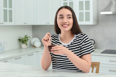 Happy woman with tasty yogurt in kitchen