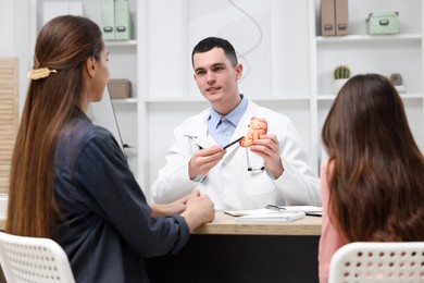 Photo of Gastroenterologist with model of stomach consulting woman and her daughter in clinic