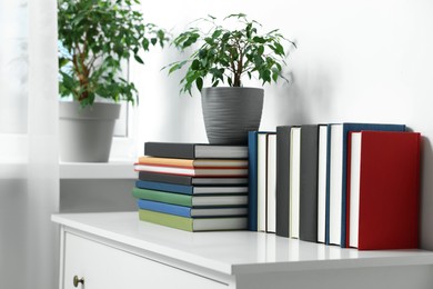 Many different books and potted plants on white cabinet indoors