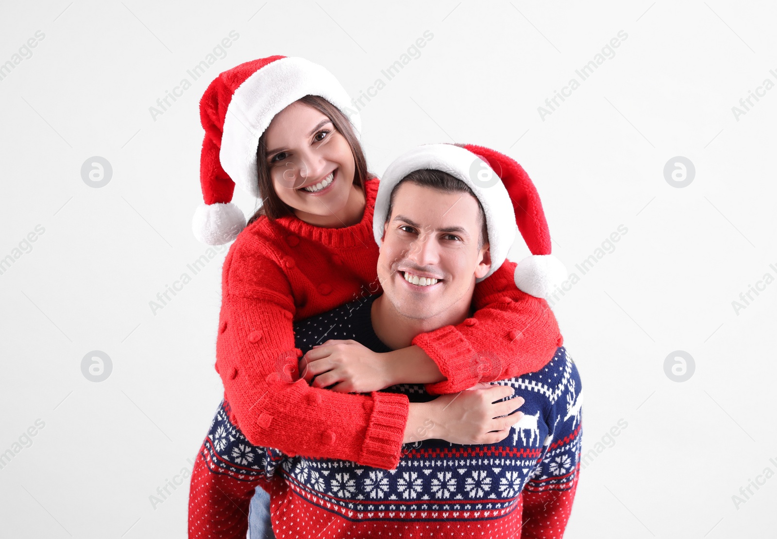 Photo of Beautiful happy couple in Santa hats and Christmas sweaters on light background