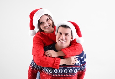 Beautiful happy couple in Santa hats and Christmas sweaters on light background