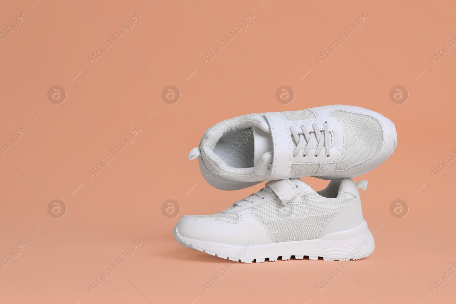 Photo of Pair of comfortable sports shoes on pale coral background. Space for text