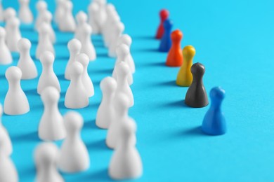 Photo of Colorful pawns on light blue background, closeup. Social inclusion concept