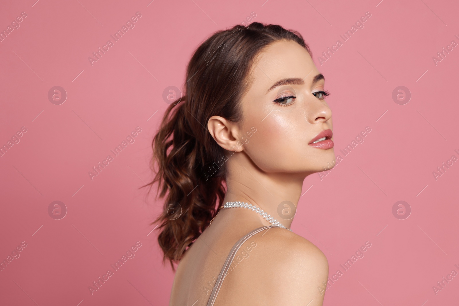 Photo of Young woman wearing elegant pearl necklace on pink background